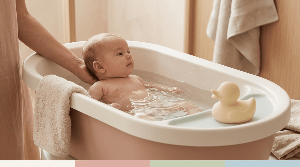 Un bébé souriant prend son bain dans une baignoire adaptée, entouré d'accessoires doux et sécurisés, dans une ambiance pastel.