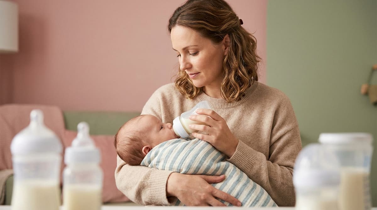 Mère offrant un biberon à son bébé dans une ambiance douce et pastel.