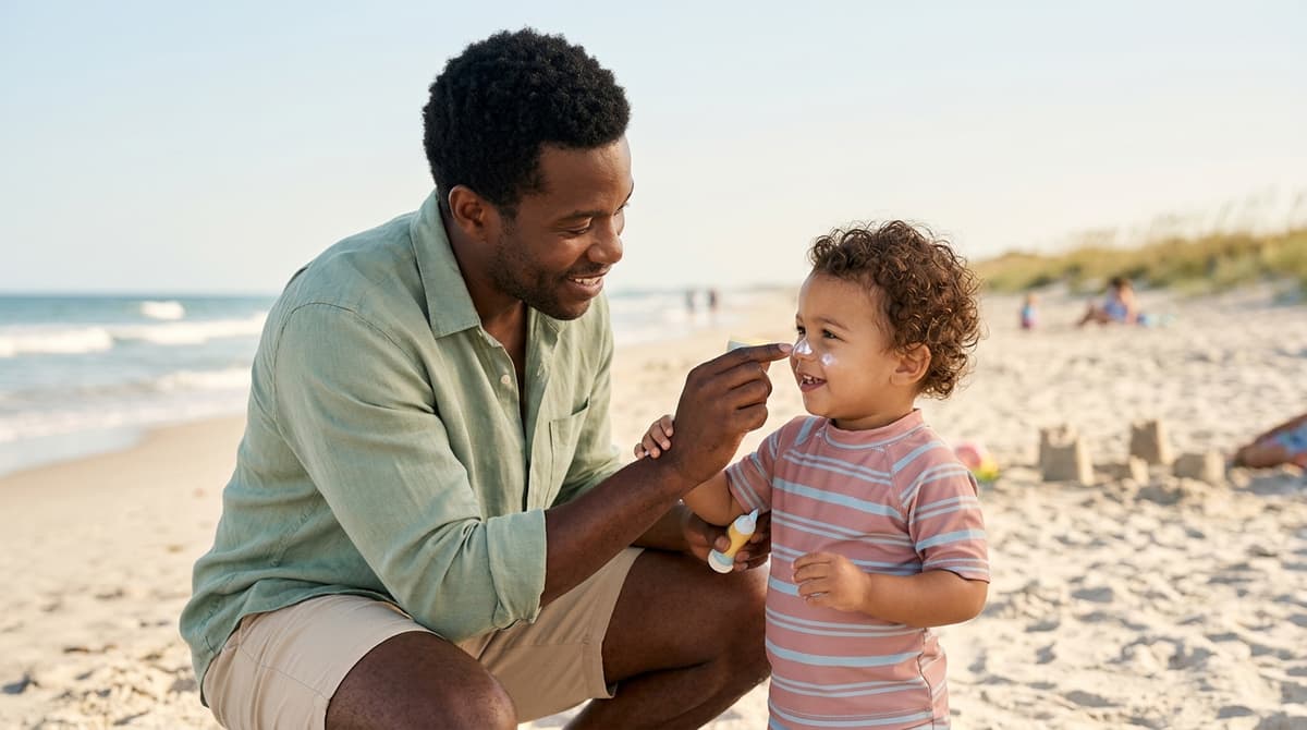 Papa appliquant de la crème solaire sur le visage de son bébé à la plage en été